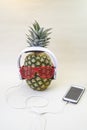 Pineapple with disco party glasses, white headphones and smartphone