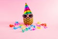 Pineapple with hat, glasses and colorul party streamers on pink background. Minimal party and celebration concept