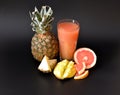 Pineapple juice with grapefruit and mango in a tall faceted glass on a black background, next to pieces of tropical fruits Royalty Free Stock Photo