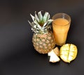 Pineapple juice with the mango in a tall faceted glass on a black background, next to pieces of tropical fruits Royalty Free Stock Photo