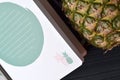 Pineapple and notebook on the dark blue wooden table.