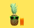 Pineapple with sunglasses and glass fruit juice on yellow background