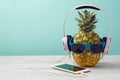 Pineapple with sunglasses, headphones and smart phone on wooden table over mint background. Tropical summer vacation Royalty Free Stock Photo