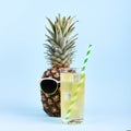 Pineapple in sunglasses and juice in a glass, concept of a funny summer mood, on a blue background