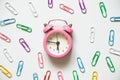 A pink alarm clock around multicolored paper clips lies on a white background, time Royalty Free Stock Photo