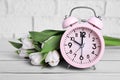 Pink alarm clock and beautiful tulips on white wooden table against brick wall, closeup. Spring time Royalty Free Stock Photo