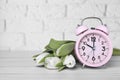 Pink alarm clock and beautiful tulips on white wooden table against brick wall, space for text. Spring time Royalty Free Stock Photo