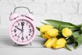 Pink alarm clock and beautiful tulips on white wooden table against brick wall. Spring time Royalty Free Stock Photo