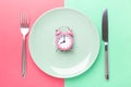 Pink alarm clock, fork, knife and empty plate on colored paper background. Intermittent fasting concept Royalty Free Stock Photo