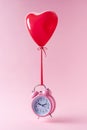 Pink alarm clock with red heart shaped balloon on pastel pink background. Minimal concept Royalty Free Stock Photo