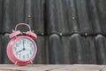 Pink alarm clock rests on an old wooden balcony and blurred background of gray tiled roof. classic style alarm clock is placed on Royalty Free Stock Photo