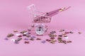 Pink alarm clock and shopping cart filled with school pencils with scattered letters on a pink background.