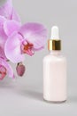 Pink anti-aging collagen, facial serum in transparent glass bottle with gold pipette and natural orchid flower on grey background Royalty Free Stock Photo