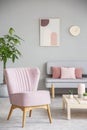 Pink armchair next to table in grey apartment interior with post