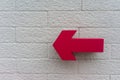 Pink arrow sign hanging against white bricks wall