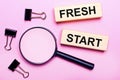 On a pink background, a magnifier, black paper clips and wooden blocks with the text FRESH START. Business concept