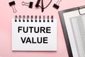 On a pink background, reports, black paper clips, glasses and a white notebook with the text FUTURE VALUE