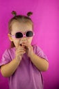 On a pink background, a stylish girl child eats coffee in sunglasses. Funny baby laughs on a pink background. Cute baby Royalty Free Stock Photo