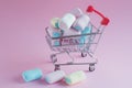 On a pink background a toy cart from a supermarket. It has a blue and pink marshmallow and three more lie side by side. Idea -