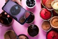 On a pink background a woman`s hand shoots cupcakes on a smartphone camera with chocolate and berries