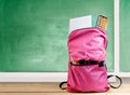Pink backpack with book and different stationery on the wooden table