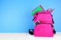 Pink backpack full of school supplies against a blue background with copy space