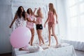Pink balloon on the left side. Confetti in the air. Young girls have fun on the white bed in nice room Royalty Free Stock Photo