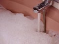 Pink Bathtub Filled to the Brim: Metallic Tap Flows with Water and Abundant Foam Royalty Free Stock Photo