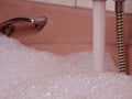 Pink Bathtub Filled to the Brim: Metallic Tap Flows with Water and Abundant Foam Royalty Free Stock Photo