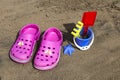 Pink beach crocs and blue sand toys on sandy beach.Beach flip flops in the foreground and blurred sea in the background
