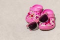 Pink beach kid`s crocs / sandals and sunglasses on sandy beach. Royalty Free Stock Photo