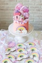 Pink birthday cake with fondant unicorn, rainbow and meringue clouds. Candy bar with cake, cookies and lollipops