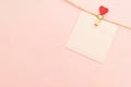 Pink blank paper sheet on a clothes line and clothespegs with red heart on a pink background. Valentines day concept Royalty Free Stock Photo