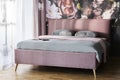 Pink blanket and grey cushions on bed in bright bedroom interior with flower print on the wall. Real photo