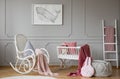 Pink blanket on rocking chair next to cradle in grey kid`s bedroom interior with poster. Real photo Royalty Free Stock Photo