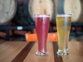Pink and blond tall cold glasses of beer on table in front of barrels in brewery