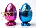Pink and blue foil wrapped Easter eggs stand ready. One pink egg has rope bow tie, blue egg cracked open. Both eggs contain Royalty Free Stock Photo