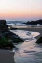 Pink and blue sunset sky, beautiful ocean, sand  and green rocks Royalty Free Stock Photo