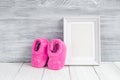 Pink booties and photo frame on wooden background