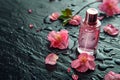 Pink bottle of perfume on background of black wet stone and flowers Royalty Free Stock Photo