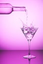 Pink bottle spilling liquid into a cocktail glass and making splash. Pink background, alcoholic drinks and cocktails concept Royalty Free Stock Photo