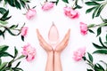 Pink bottle of women`s perfume in female hands and peony flowers around on white background. Spring gentle fragrance for