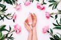 Pink bottle of women`s perfume in female hands and peony flowers around on white background. Spring gentle fragrance for Royalty Free Stock Photo