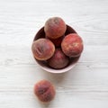 Pink bowl of fresh peaches on a white wooden background, overhead. Top view. Royalty Free Stock Photo