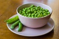 Pink bowl with green peas and three pea pods lie near Royalty Free Stock Photo