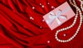 Pink box with a ribbon and a string of pearls on a red background Royalty Free Stock Photo