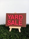 Pink and brown yard sale sign on a wood easel on green grass
