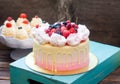 Pink cake with melted chocolate, strawberry, blueberry and cherry and cupcakes with whipped cream and fresh berries