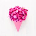 Pink carnation flowers bouquet in a pink cone on a white wooden background. Greeting card. Flat lay Royalty Free Stock Photo