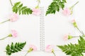 Pink carnation flowers and green leaves placed around blank notebook on white background